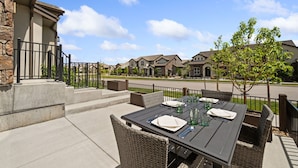 An outdoor patio with a table set for dining, stone steps, and a view of residential buildings. - The Highland Retreat | Gym, Sauna, Pool & Spa (Windsor)