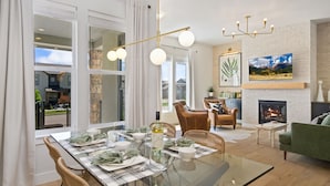 A dining area with a glass table set for four, a fireplace, and a television mounted on the wall. - The Highland Retreat | Gym, Sauna, Pool & Spa (Windsor)