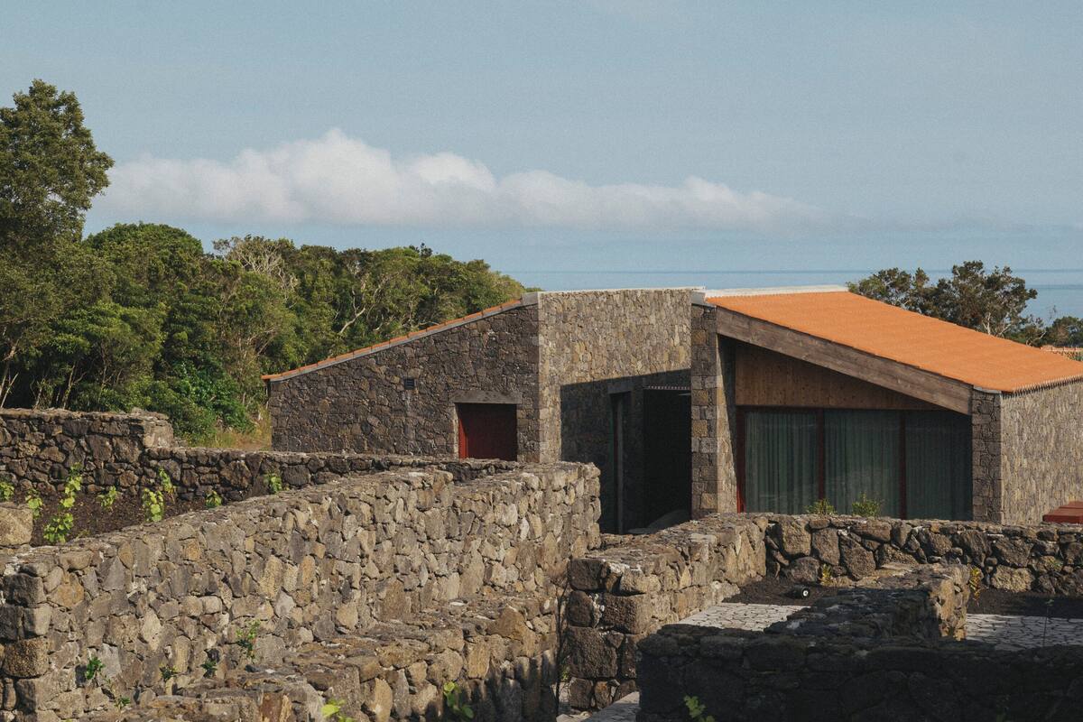 A stone building with a red roof, surrounded by greenery and a clear sky.