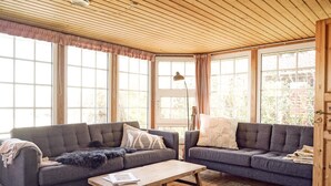 Ein gemütliches Wohnzimmer mit zwei grauen Sofas, einem Holztisch und einem großen Fenster mit Vorhängen.