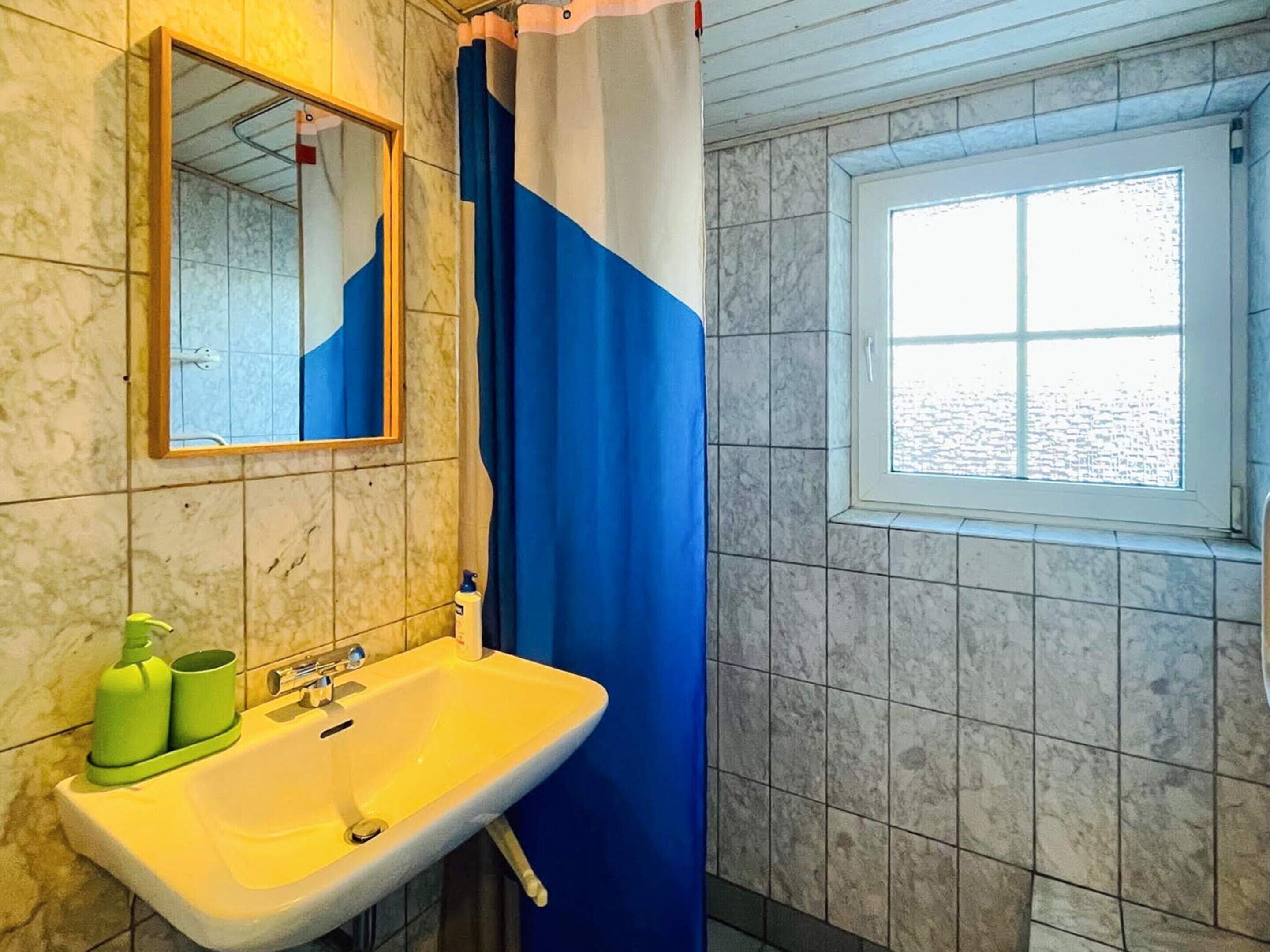 A bathroom with a sink, mirror, shower curtain, and window.