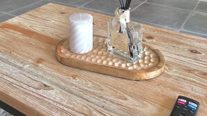 Una sala de estar moderna con un televisor montado en la pared, una consola de madera, un adorno decorativo y un control remoto sobre una mesa de centro.