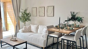 Una sala de estar acogedora con un sofá, una mesa de centro de madera y una mesa de comedor preparada para cuatro personas. Hay tres obras de arte abstracto en la pared sobre la mesa.