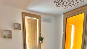 Un dormitorio con cama, almohadas, un espejo, una planta en maceta y una puerta.