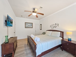 Un dormitorio con cama, ventilador de techo, televisor, un cuadro y un adorno de pared.