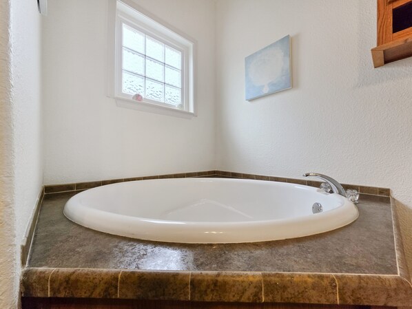 Ein Badezimmer mit einer freistehenden Badewanne, einem Fenster und einem kleinen gerahmten Kunstwerk an der Wand.