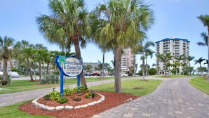 A sign for the Estero Beach & Tennis Club with a paved pathway and palm trees.