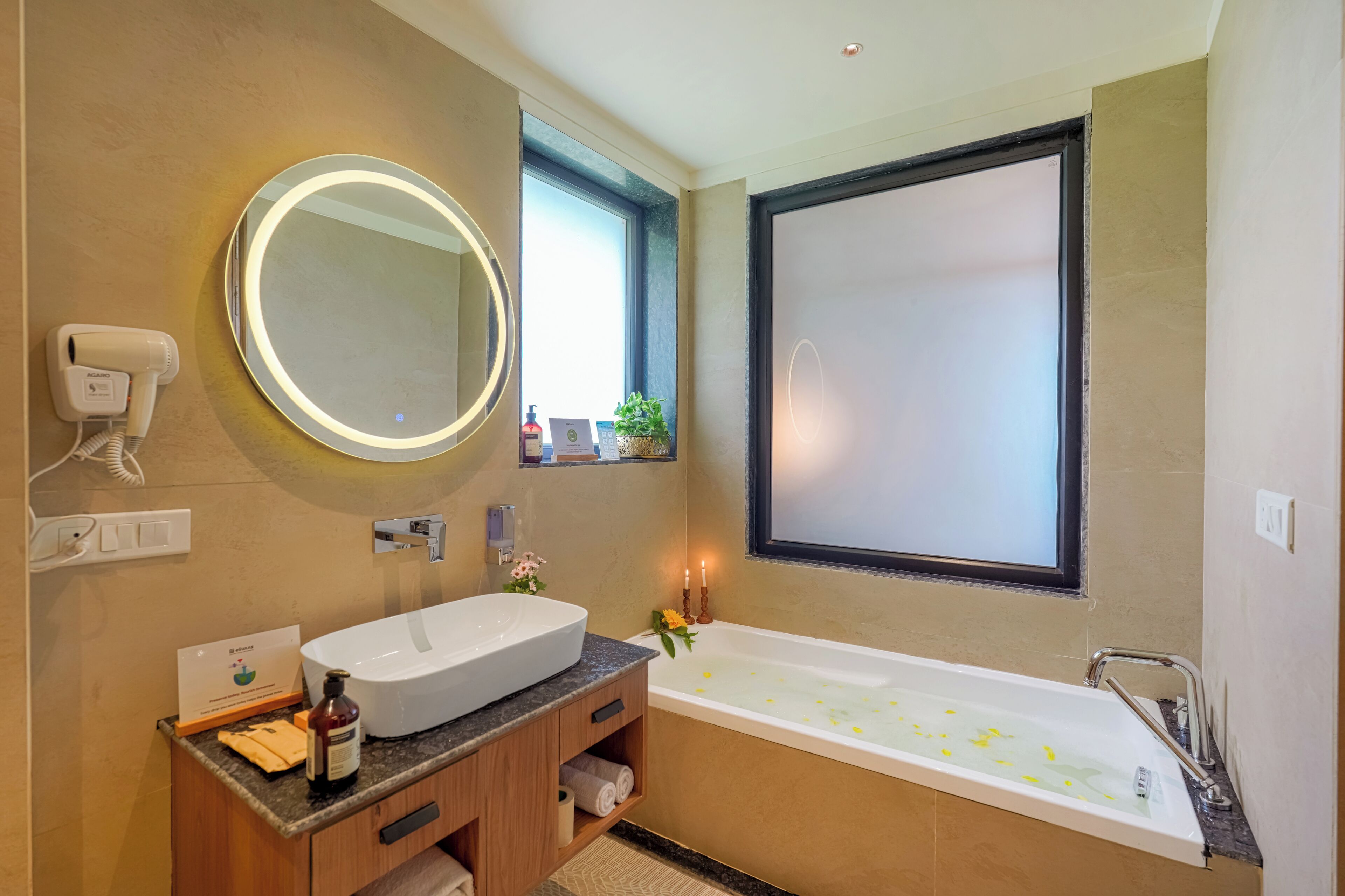 A modern bathroom with a large oval mirror, a standalone sink, and a freestanding bathtub.