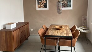 A dining area with a wooden table, leather chairs, a wooden cabinet, and two framed botanical prints on the wall. - Vacation home in Eschweiler - relaxation near the Eifel (Eschweiler)