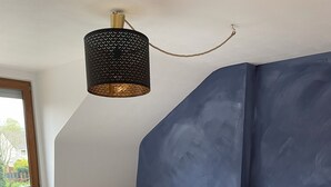 A bedroom with a wooden bed, a white bedspread, a dark blue accent wall, and a hanging lamp. - Vacation home in Eschweiler - relaxation near the Eifel (Eschweiler)