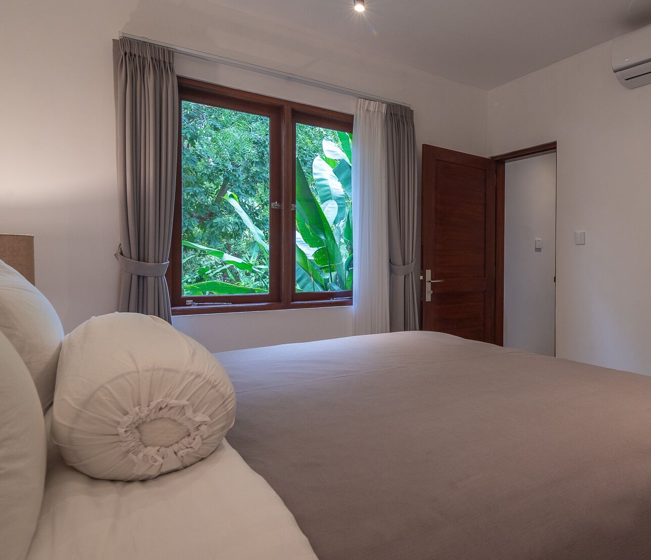 A bedroom with a bed, a wooden dresser, a window with curtains, and an air conditioning unit.
