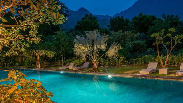 A swimming pool with lounge chairs and palm trees, surrounded by lush greenery and mountains in the background. - Luxury retreat resort in Natural Harmony in Pemuteran! (bali)