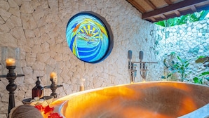 A stone-walled bathroom with a large bathtub, a stained glass window, and a stone archway. - Luxury retreat resort in Natural Harmony in Pemuteran! (bali)