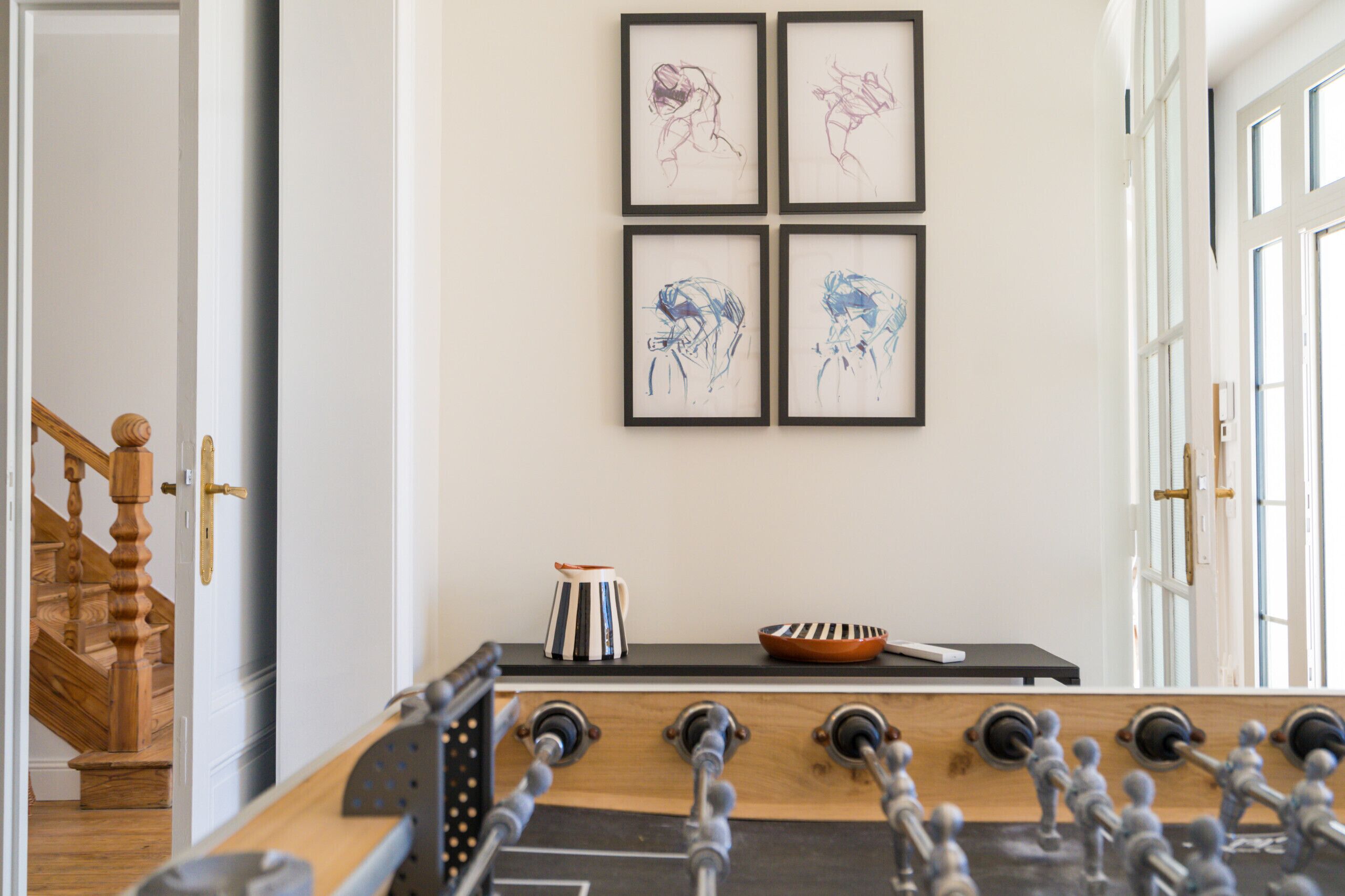 A room with a foosball table, a wooden staircase, and four framed artworks on the wall.
