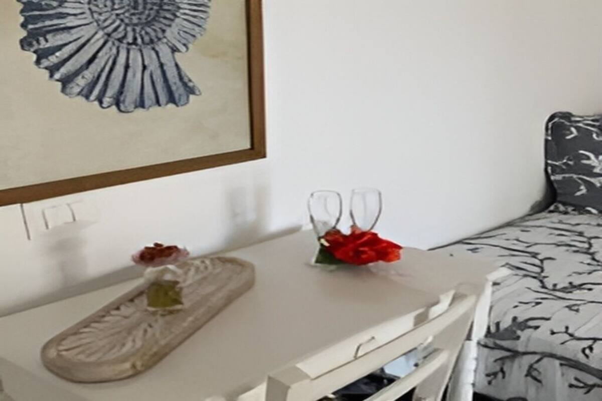 Ein weißer Nachttisch mit einer dekorativen Ablage, einem gerahmten Kunstwerk und zwei Glasvasen mit Blumen.