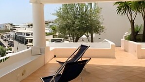 Un balcón con una única silla de descanso, piso de baldosas y vista panorámica de la ciudad.