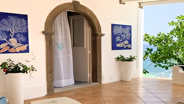 Una habitación amplia con un gran arco que da a un balcón, suelo de baldosas y dos macetas.