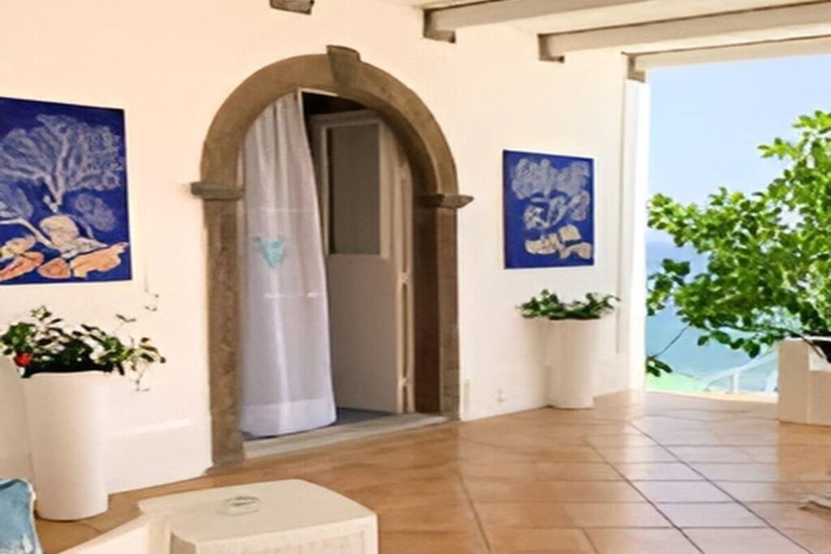 Ein geräumiges Zimmer mit einem großen, rundbogenförmigen Durchgang zu einem Balkon, Fliesenboden und zwei Blumentöpfen.