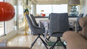 A modern dining area with grey upholstered chairs, a round table with a blue and white patterned tablecloth, and a decorative vase with white flowers. - Appartement 145m², Vue Mer, Parking, Accès Plage (Arcachon)