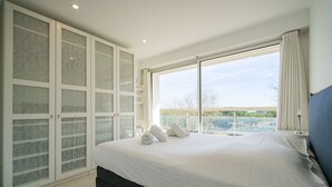A bedroom with a large bed, a wardrobe with frosted glass doors, and a balcony with a view. - Appartement 145m², Vue Mer, Parking, Accès Plage (Arcachon)