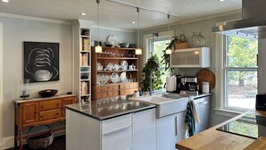 A modern kitchen with a central island, white cabinetry, and a view of the outdoors through a large window. - In Town Delight! (Manchester)