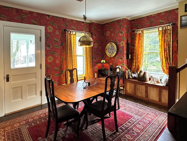A dining room with a wooden table and chairs, floral wallpaper, and a window with curtains. - In Town Delight! (Manchester)