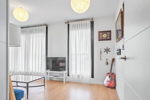 Una sala de estar moderna con un televisor sobre un mueble blanco, una guitarra apoyada en la pared y una mesa de comedor con una silla azul.