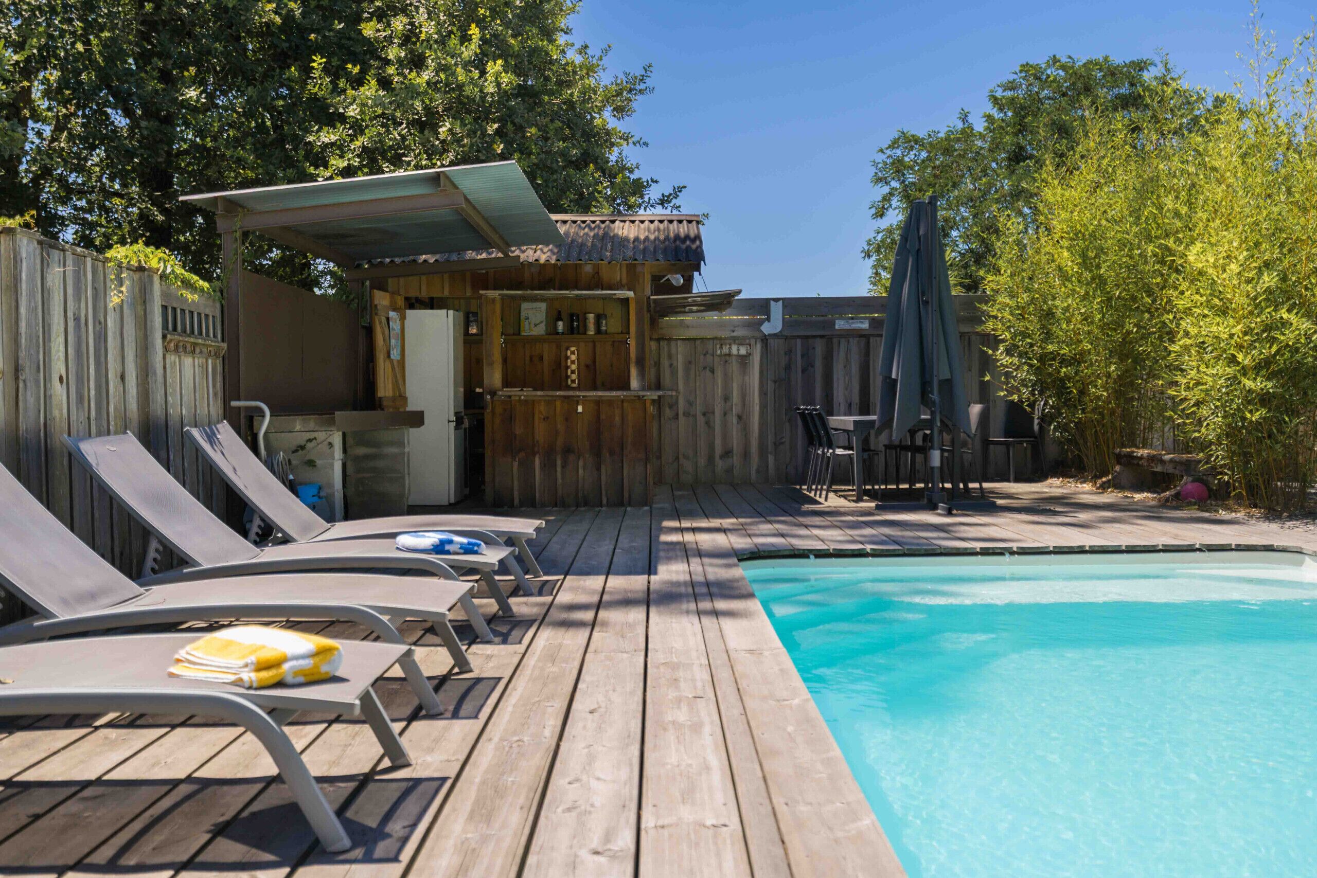 A wooden deck with a pool, lounge chairs, and a bar area.
