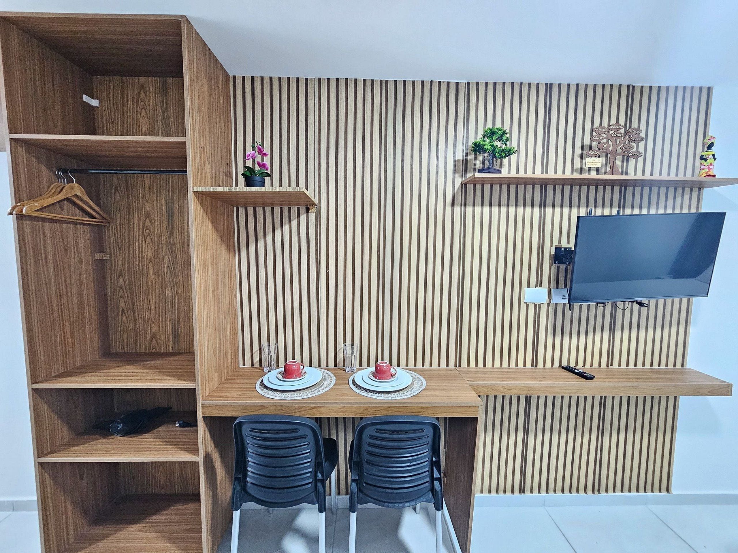 Una habitación compacta con escritorio de madera, dos sillas, un televisor y adornos en estanterías.