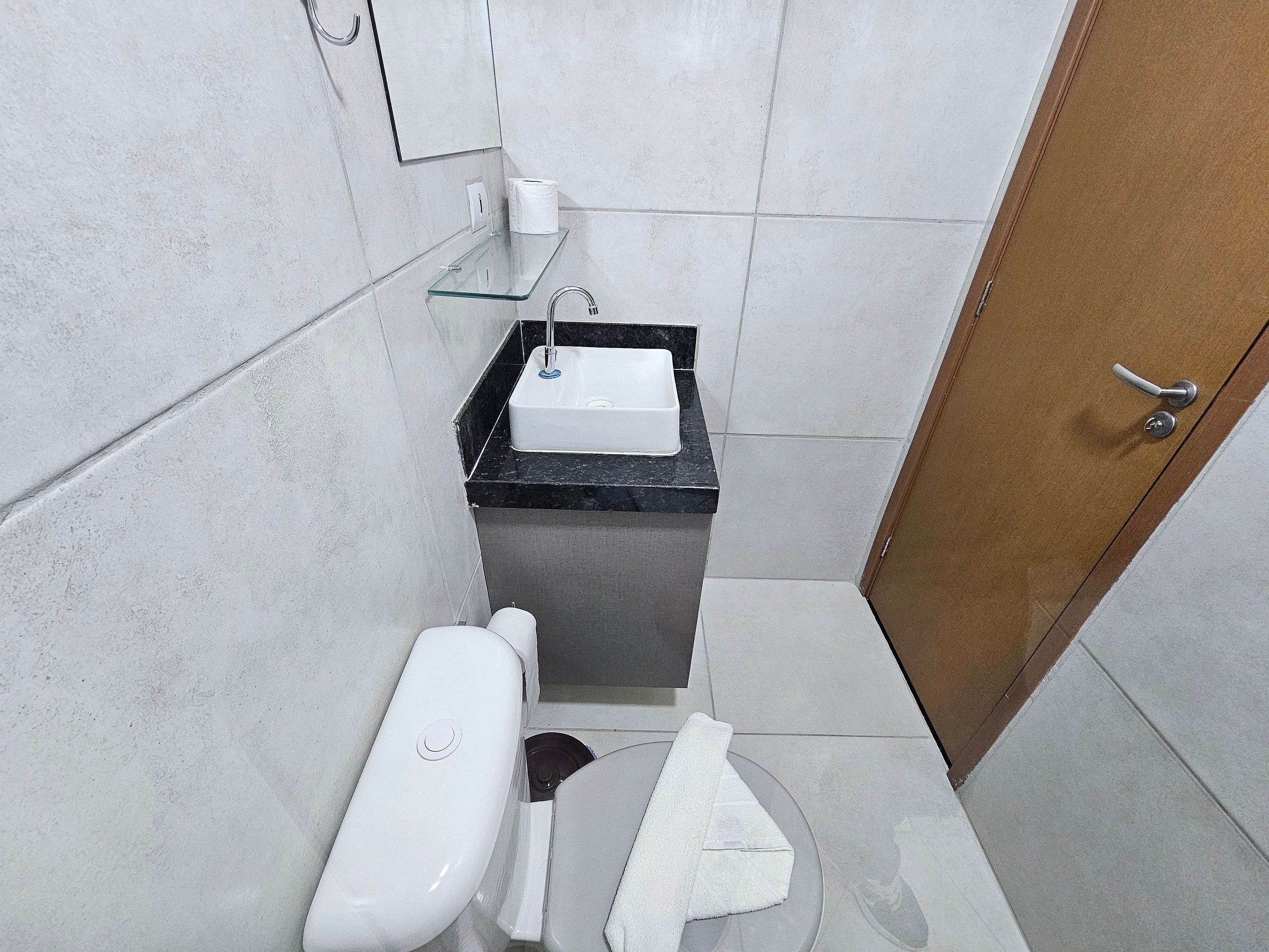 Un baño pequeño con un inodoro blanco, un lavamanos con encimera negra y una puerta de madera.