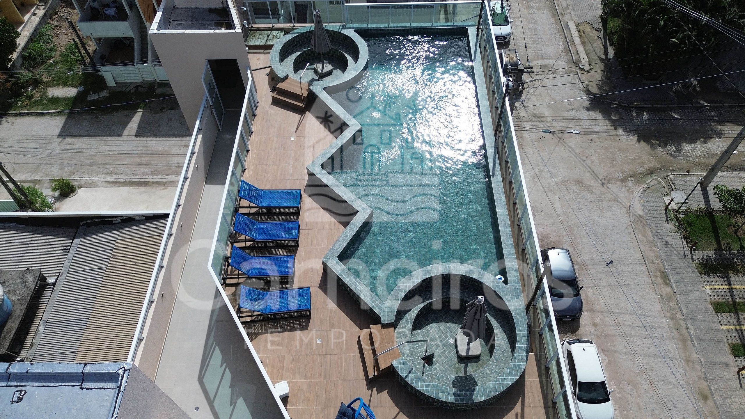 An aerial view of a rooftop pool with a circular design, blue lounge chairs, and a small circular seating area.