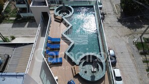 An aerial view of a rooftop pool with a circular design, blue lounge chairs, and a small circular seating area. - Eco Mirage Residence (Ipojuca)