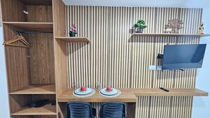 A compact room with a wooden desk, two chairs, a TV, and decorative items on shelves. - Eco Mirage Residence (Ipojuca)