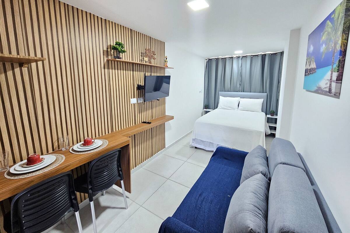 Ein Hotelzimmer mit einer Wand aus Holzlatten, einem daran befestigten Fernseher, einem Bett mit weißen Laken, einem blauen Sofa und einem kleinen Tisch mit einer roten Tasse und einem Untertasse.