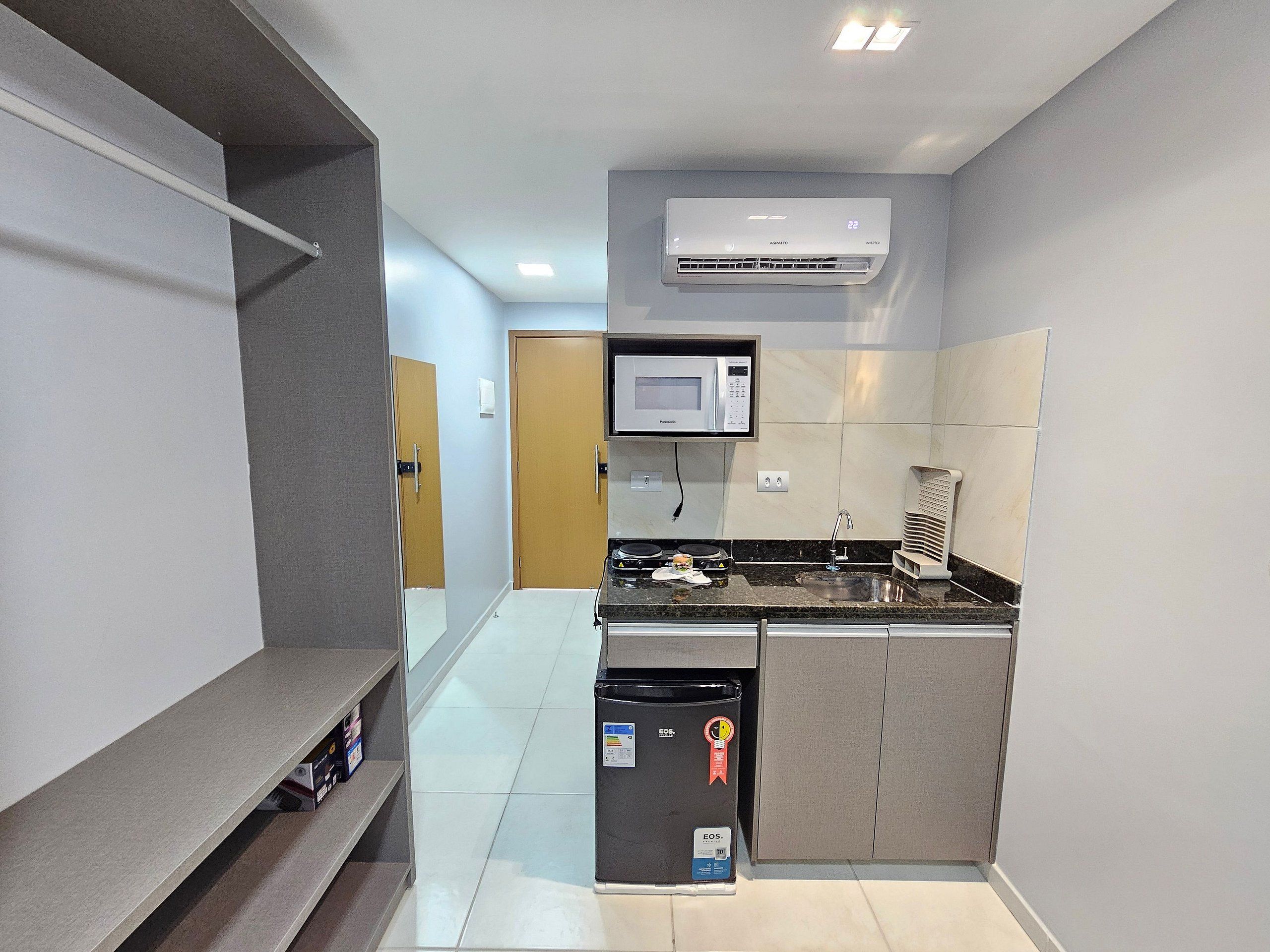 A compact kitchen with a microwave, stove, sink, and an air conditioner.