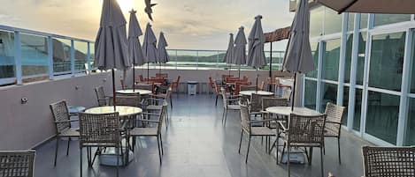 A rooftop terrace with outdoor seating, including wicker chairs and tables, and umbrellas providing shade.