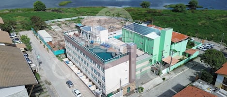 A multi-story building with a rooftop pool, surrounded by greenery and a body of water.