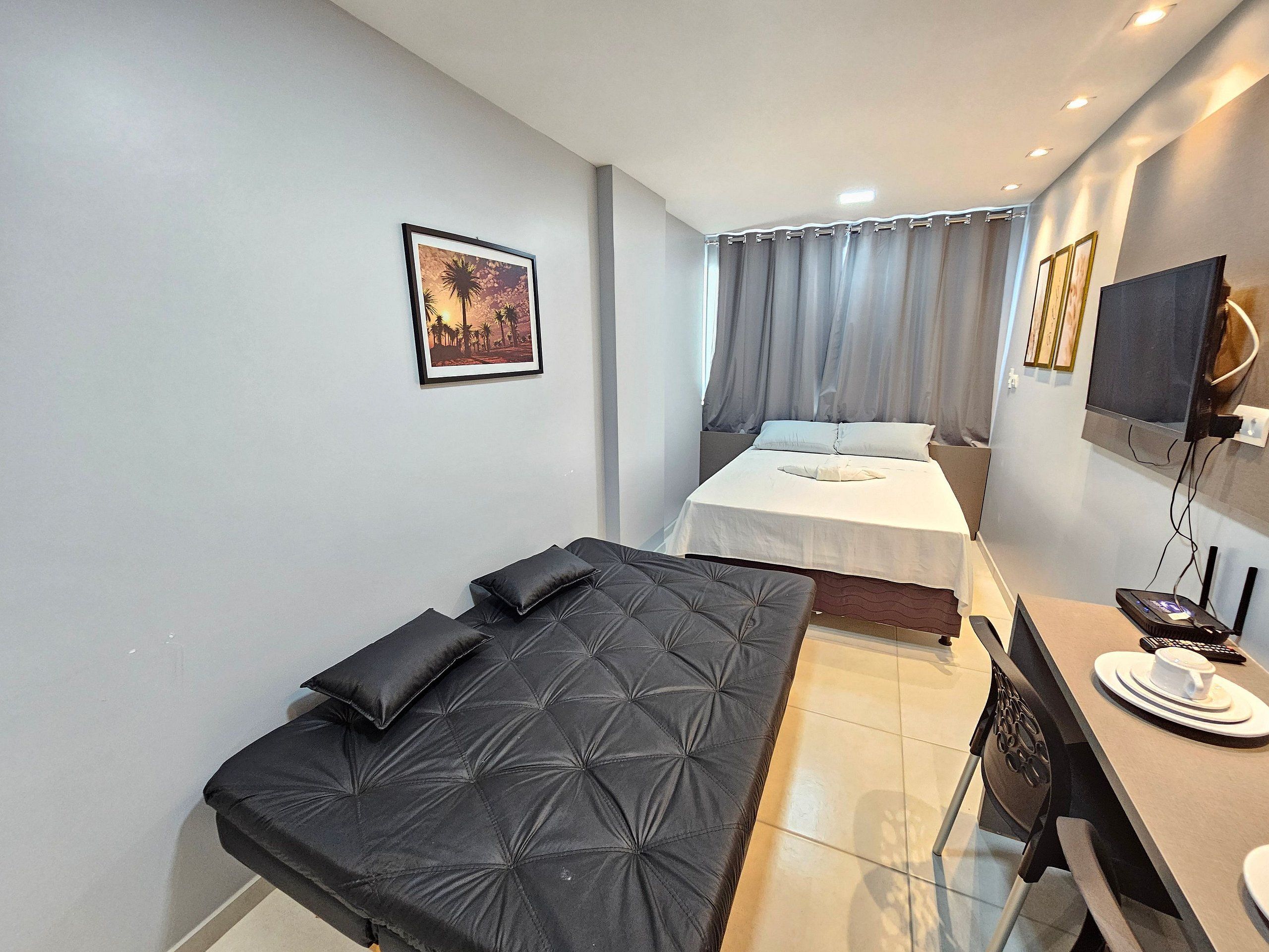 A modern hotel room with a bed, a sofa, a desk, and a TV.