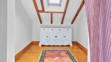 A room with a sloped ceiling, wooden beams, a white cabinet, and a patterned rug.