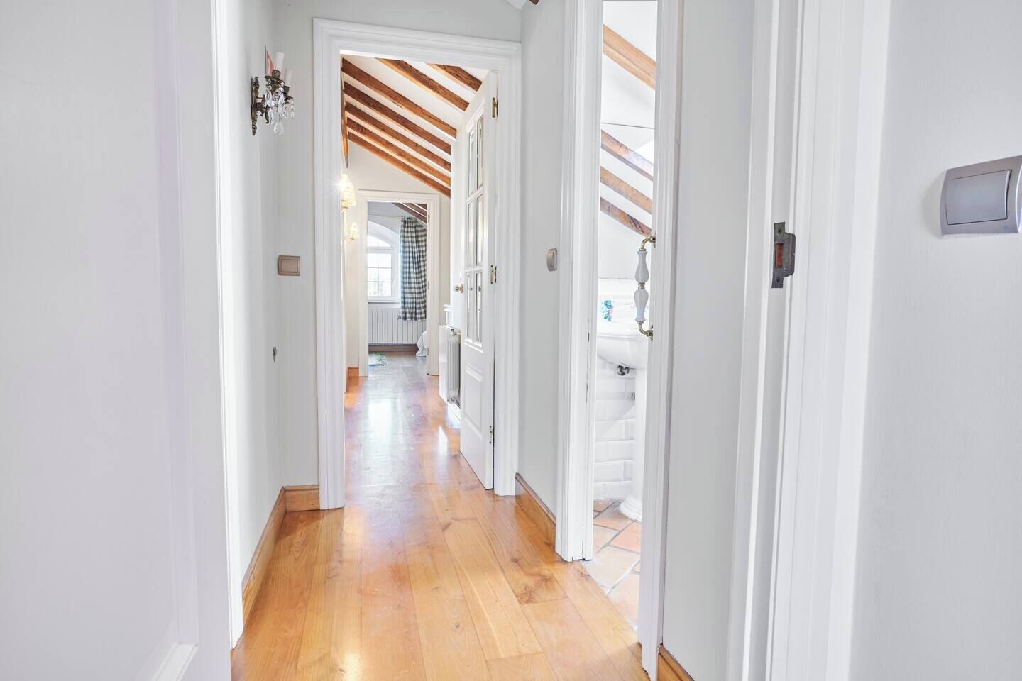 A hallway with wooden flooring and white walls, leading to a room with a window and a radiator.