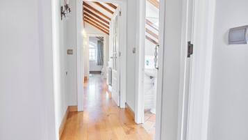 A hallway with wooden flooring and white walls, leading to a room with a window and a radiator.