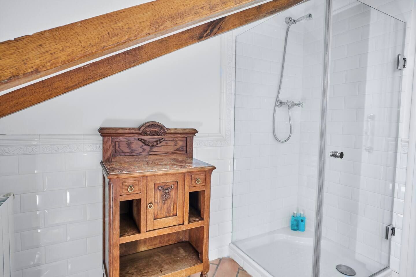 Une salle de bain avec un meuble-lavabo en bois, une douche et des murs recouverts de carreaux blancs.