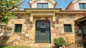 Un bâtiment en pierre avec une porte verte, deux fenêtres à l’étage et une petite fenêtre au rez-de-chaussée.