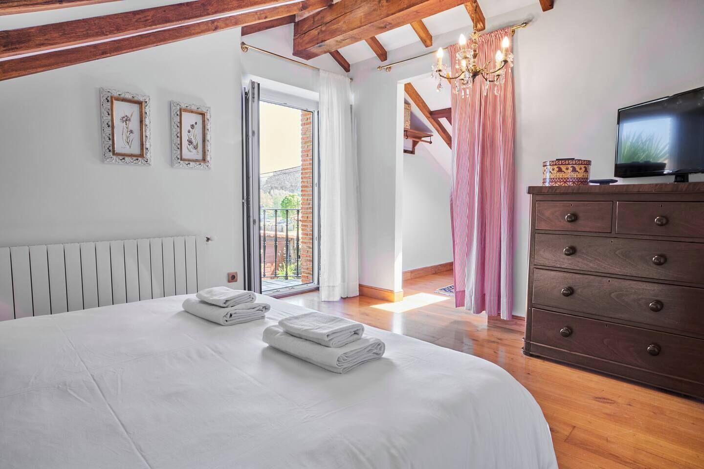 A bedroom with a bed, a dresser, a television, and a view of the outdoors.