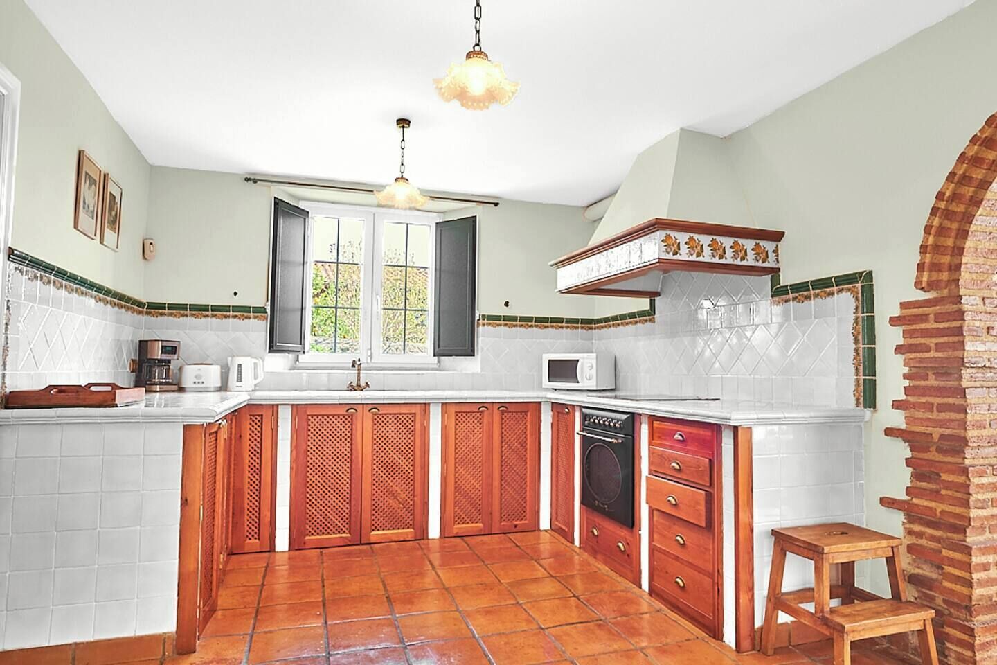Una cocina con encimera blanca, armarios de madera, microondas y una ventana con contraventanas.