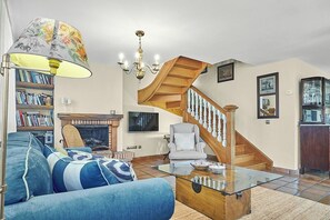A living room with a sofa, a glass coffee table, a fireplace, a bookshelf, a staircase, and a chandelier. - Casa Parbayón-Encanto entre Jardines y Luz Natural (Piélagos)