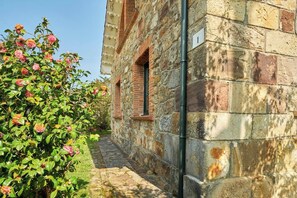 A stone building with a narrow stone pathway leading to a door, surrounded by lush greenery and flowering plants.