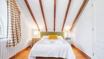 A bedroom with a bed, a headboard, a nightstand, a lamp, and a window with curtains.