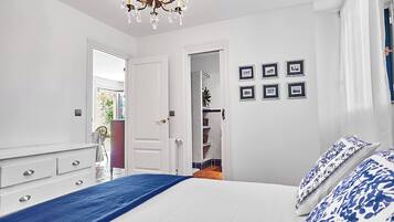 Un dormitorio con una cama, un aparador, una araña y una puerta que da a un baño.