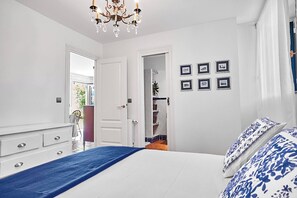 A bedroom with a bed, a dresser, a chandelier, and a door leading to a bathroom. - Casa Parbayón-Encanto entre Jardines y Luz Natural (Piélagos)